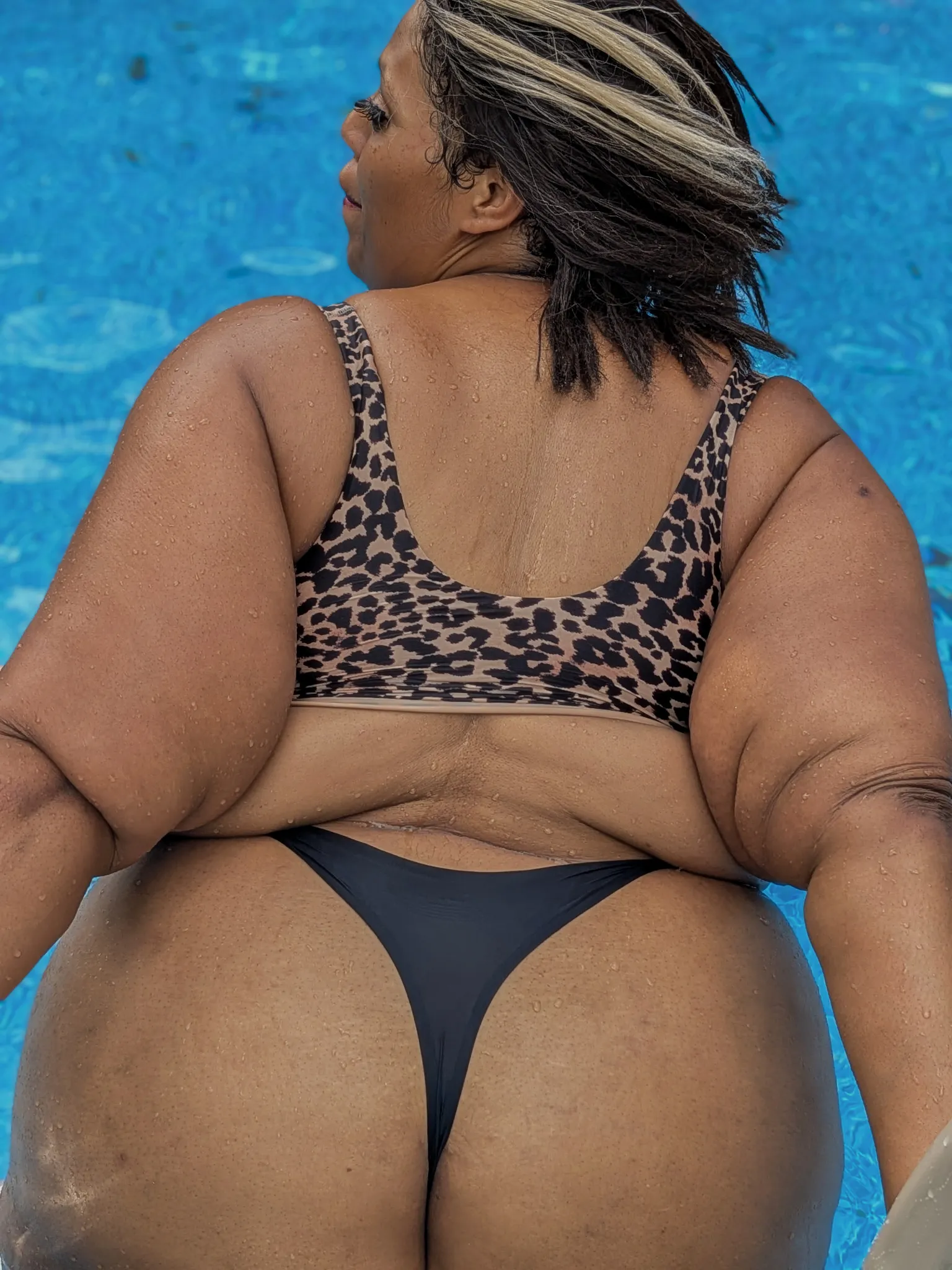 Amanda in the pool photographed from a low angle from behind, turned to look off to one side.