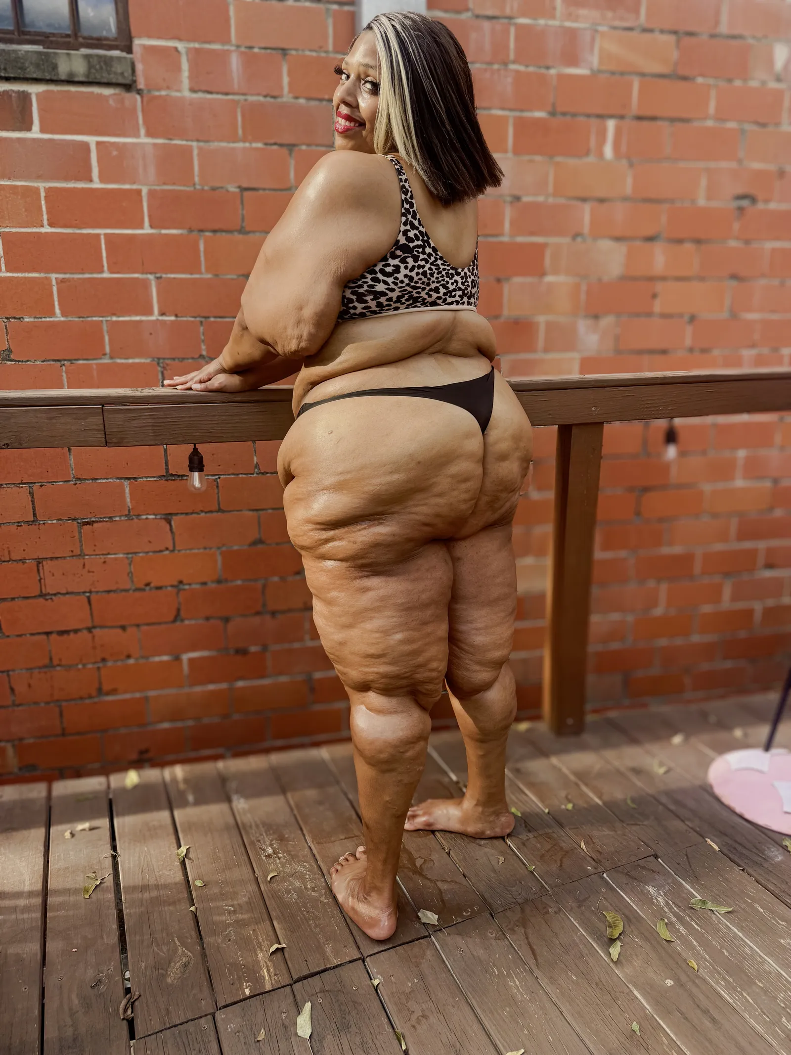 Amanda leaning on the deck rail with her back to the camera, glancing over her shoulder and smiling, bulbs strung along the rail.
