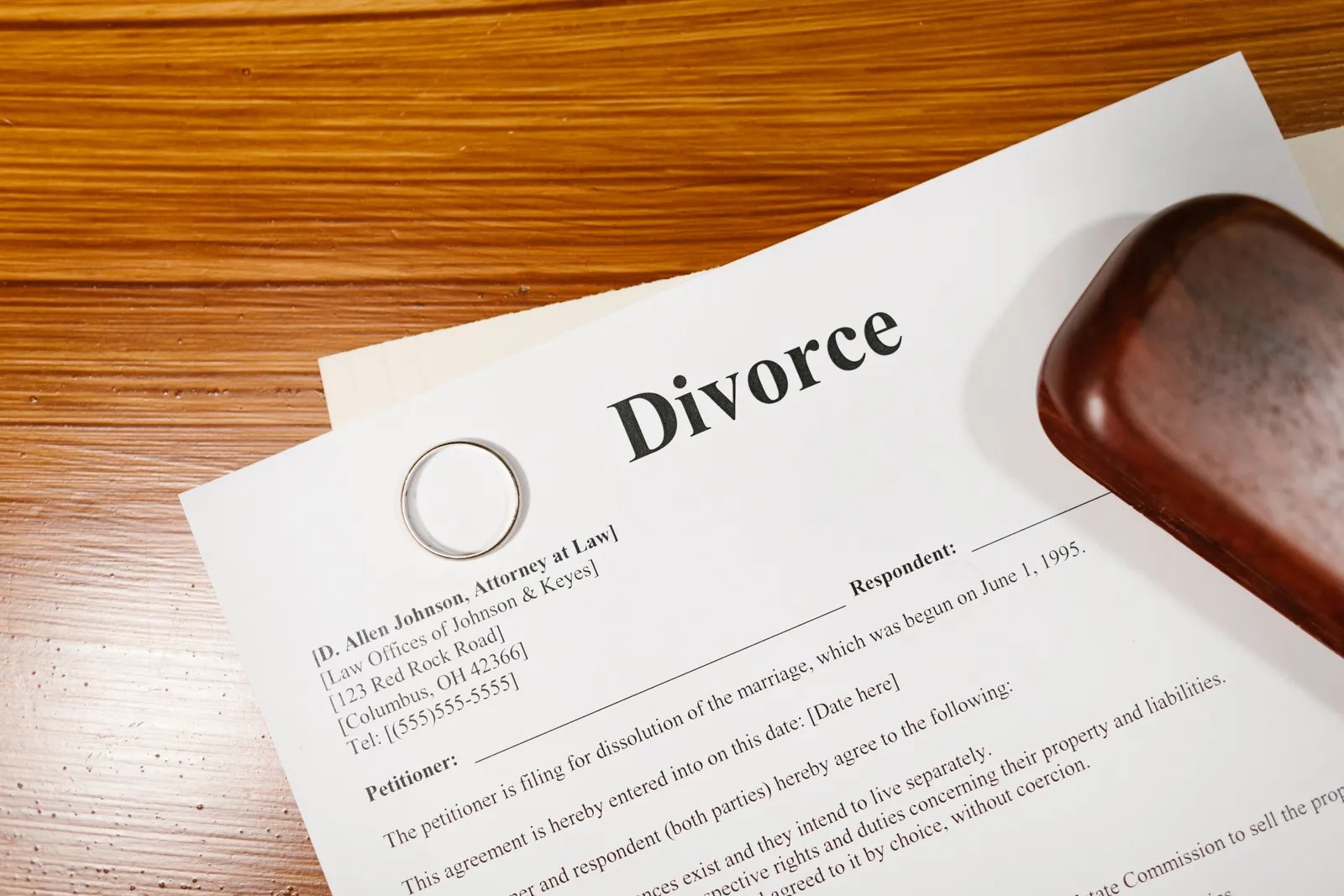 A signed divorce document and a plain gold wedding ring lying together on a wooden desk, photographed close-up.