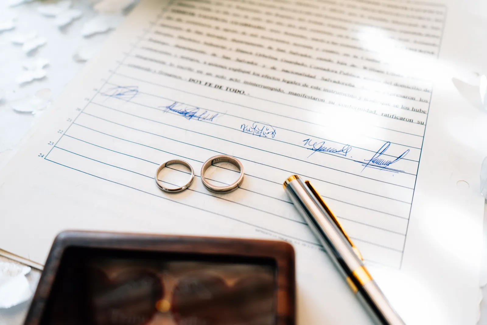 Two wedding rings resting on a signed marriage certificate, photographed close-up on a plain surface.