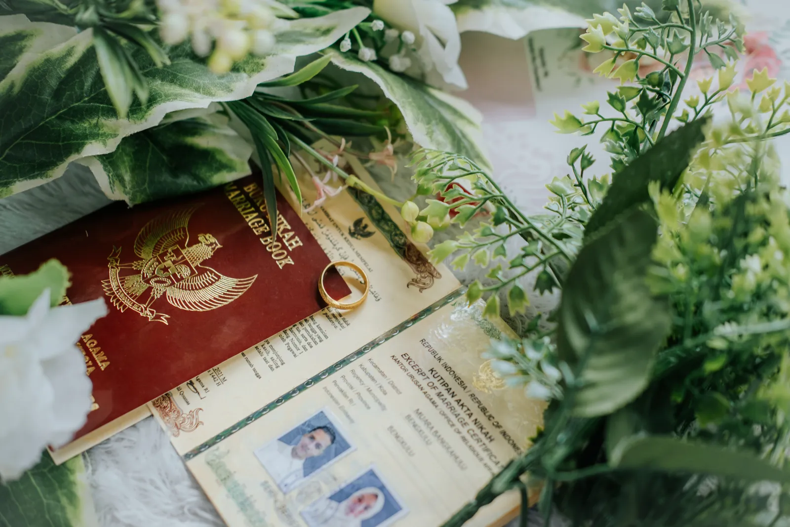 A marriage record book and certificate decorated with greenery and a wedding ring, photographed close-up.