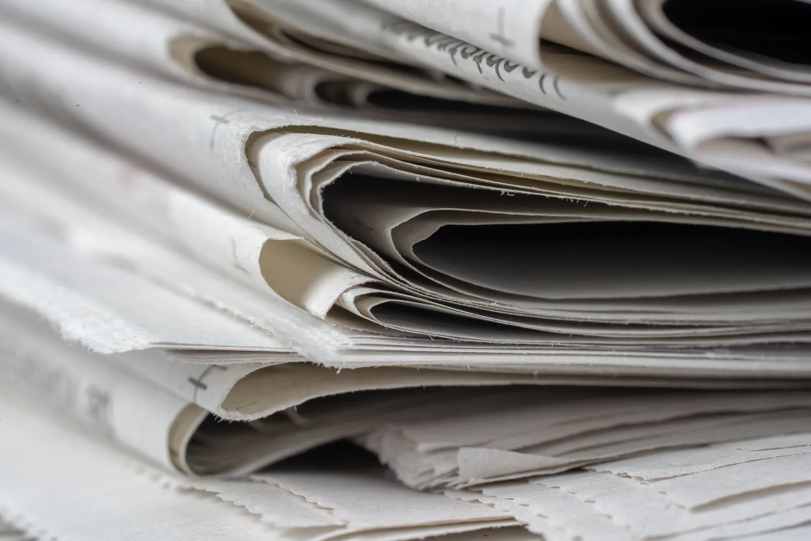 A tightly folded stack of newspapers photographed close-up, showing only paper texture and folded edges with no readable headline.