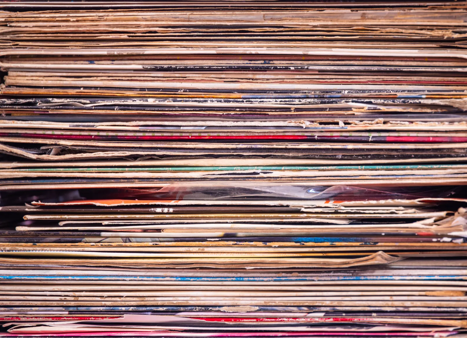 Close-up view of a stack of vintage vinyl records with colorful, worn album-cover spines. No people are depicted.
