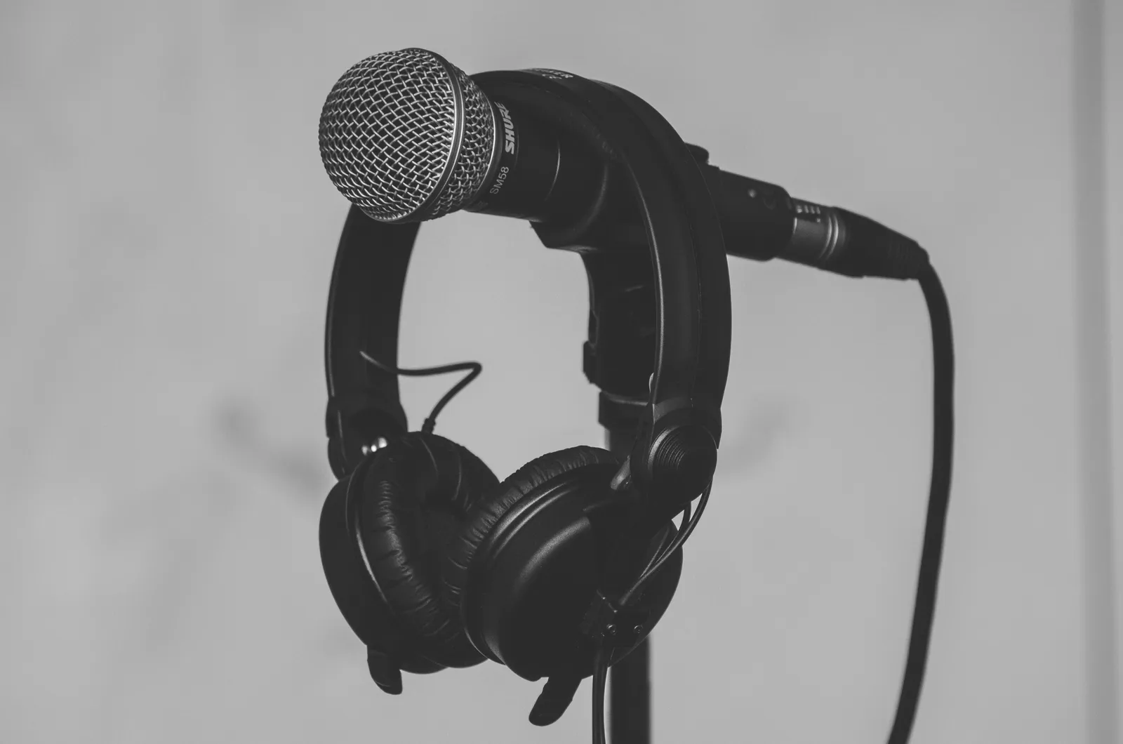Black-and-white close-up of a handheld studio microphone with a pair of headphones looped over it, mounted on a stand. No people are depicted.