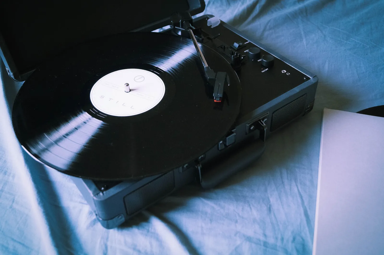 A black vinyl record spinning on a portable turntable resting on a blue textile surface. No people are depicted.