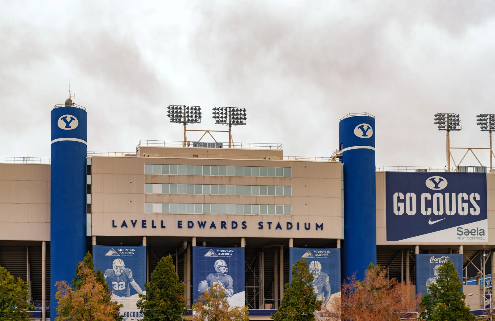 A close-up of LaVell Edwards Stadium's entrance towers, marked with BYU's "Y" logo and a "Go Cougs" banner, under an overcast sky.