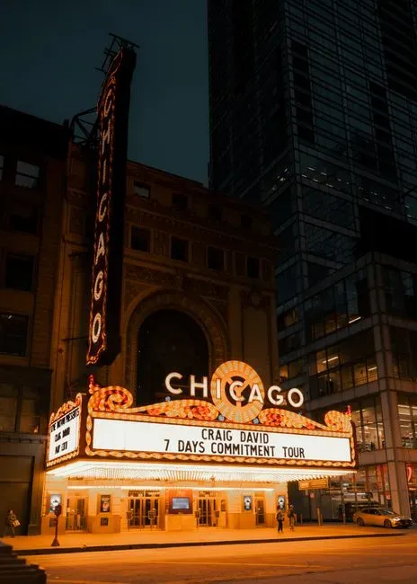 A grand theatre marquee lit up at night on a city street, its vertical sign spelling CHICAGO in white bulbs above a curved marquee edged in rows of glowing lights.