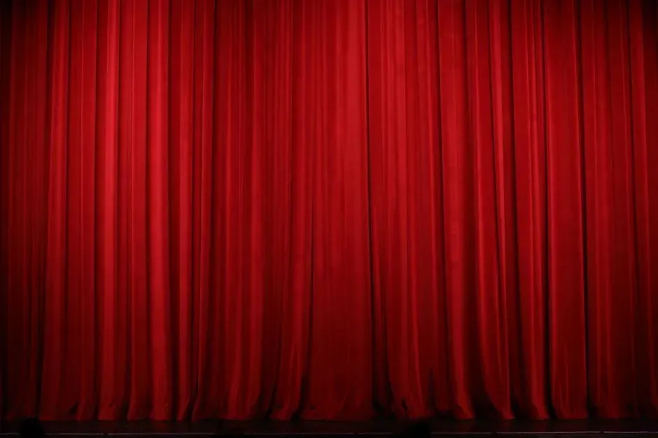 A closed red velvet stage curtain filling the frame, lit warmly so its heavy vertical folds catch the light.