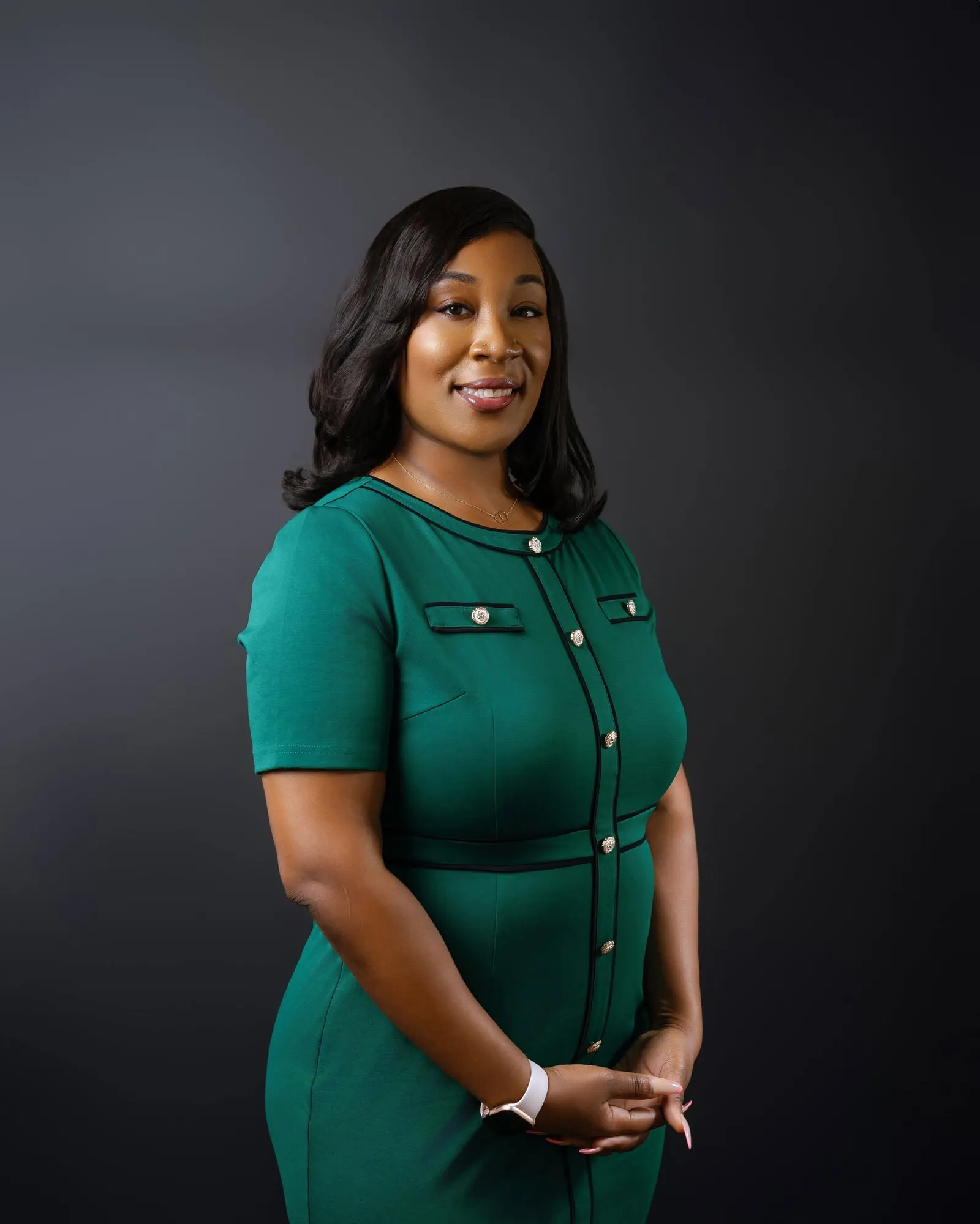 Ebony Williams, the Democratic nominee for Harris County Civil Court at Law No. 2, photographed in a green short-sleeved dress with black piping and gold buttons against a dark grey studio backdrop, hands clasped, smiling to camera.