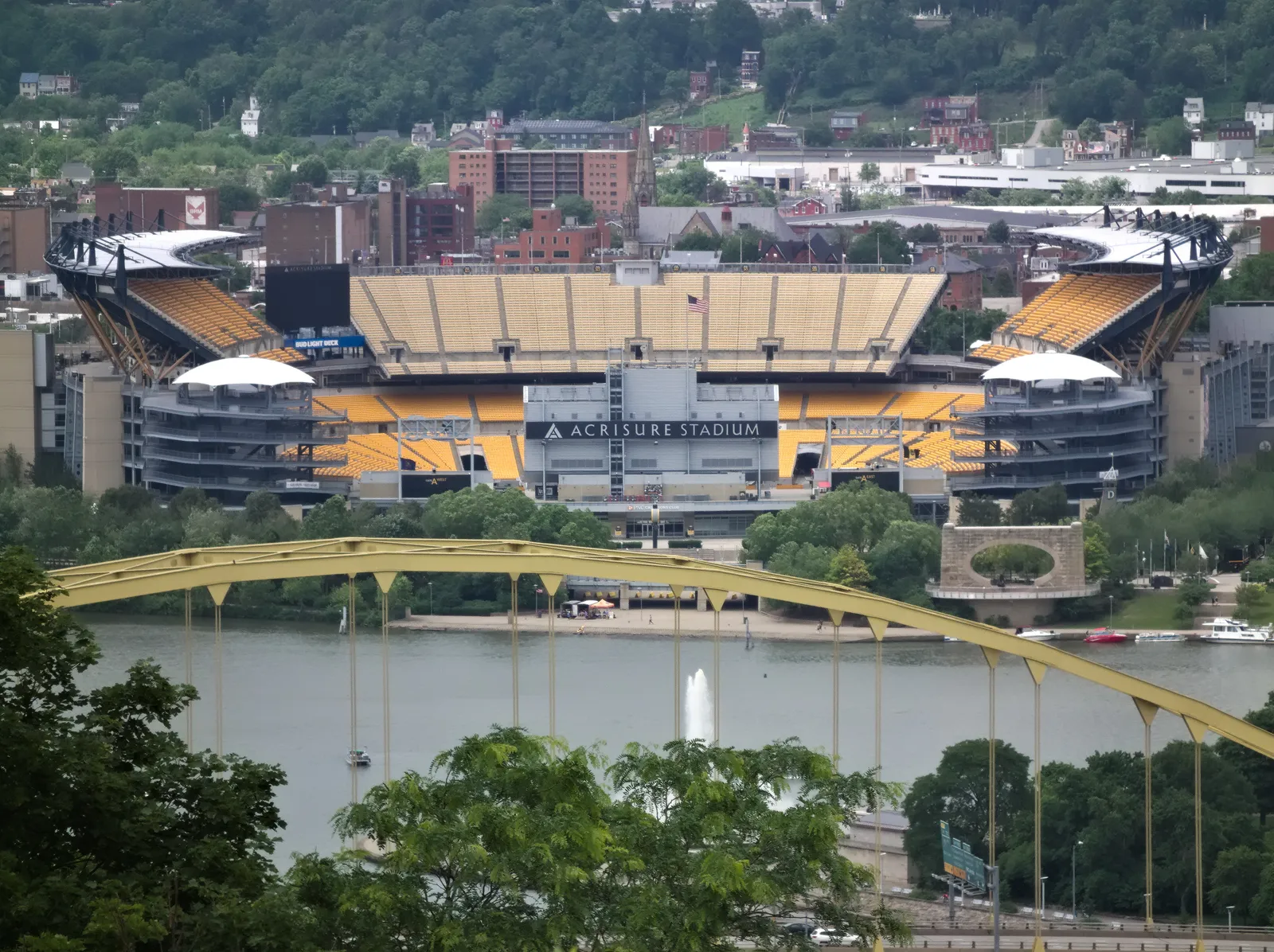 Acrisure Stadium in Pittsburgh, seen from across the Allegheny River with the Fort Pitt Bridge in the foreground, daytime, no game in progress.