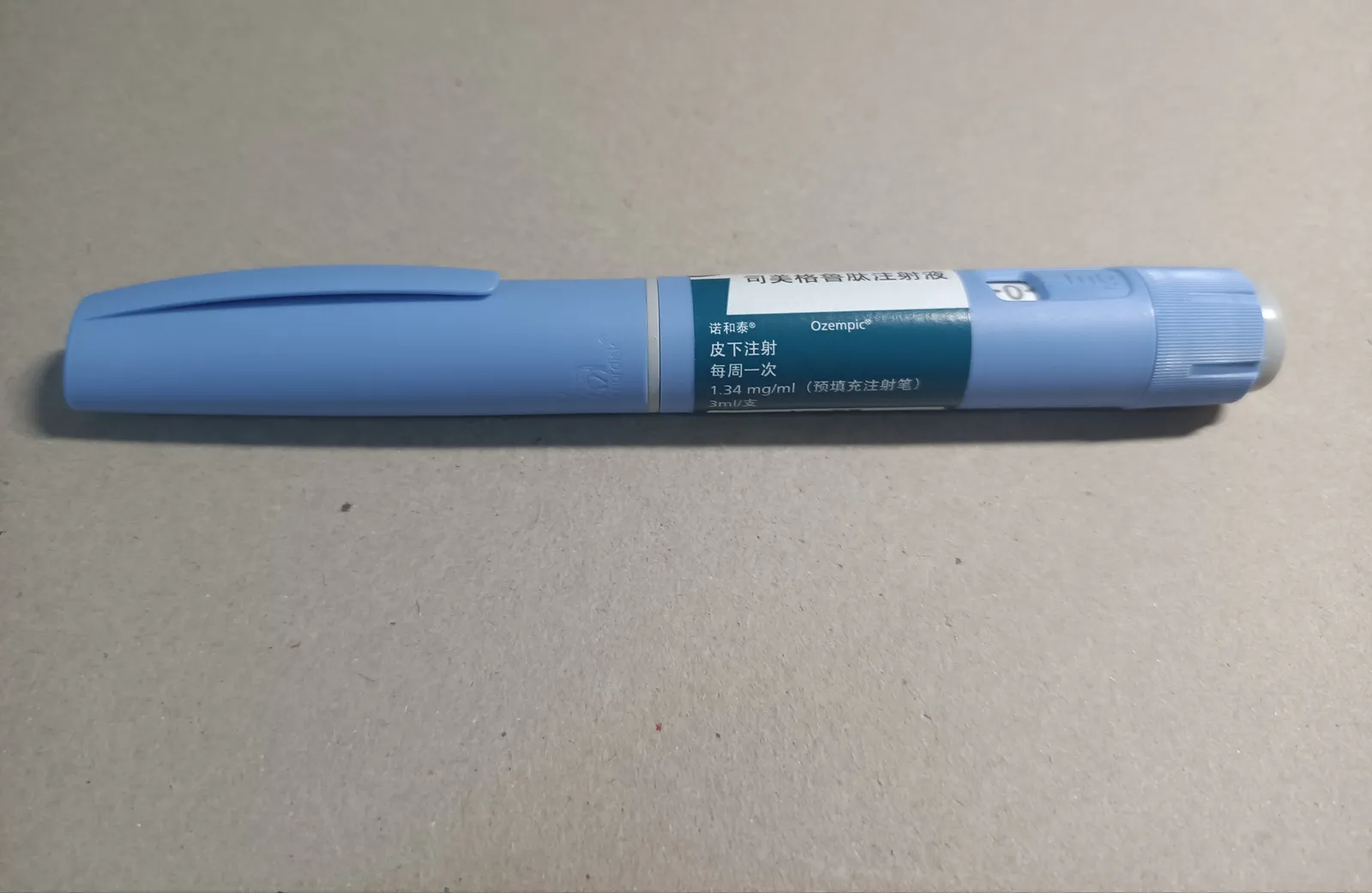 A pale blue Ozempic semaglutide injection pen lying on a plain buff-coloured surface, its label printed in Chinese and marked 1.34 mg/ml, 3 ml, with the dose window visible near the dial end.