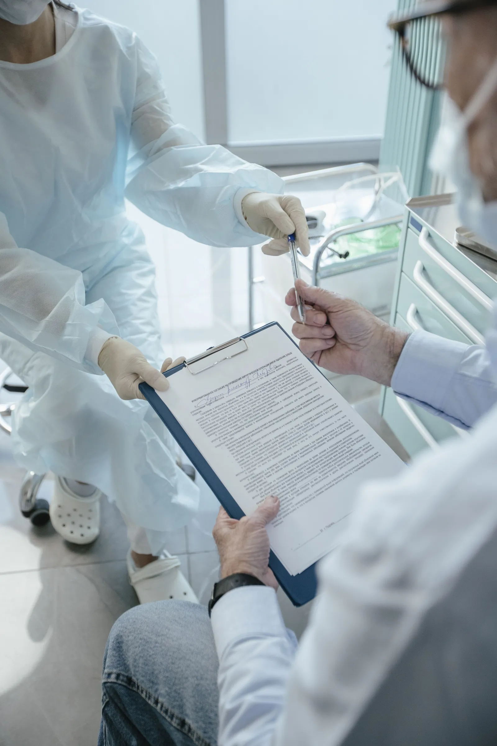 A healthcare professional's hands passing a clipboard and pen to a patient for a signature in a medical office.