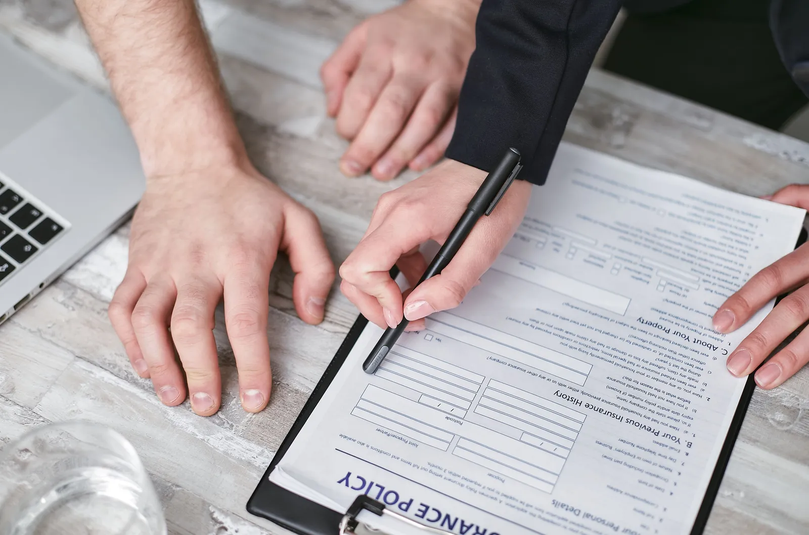 Close-up of two people's hands at a wooden desk, one holding a pen over a document being signed.