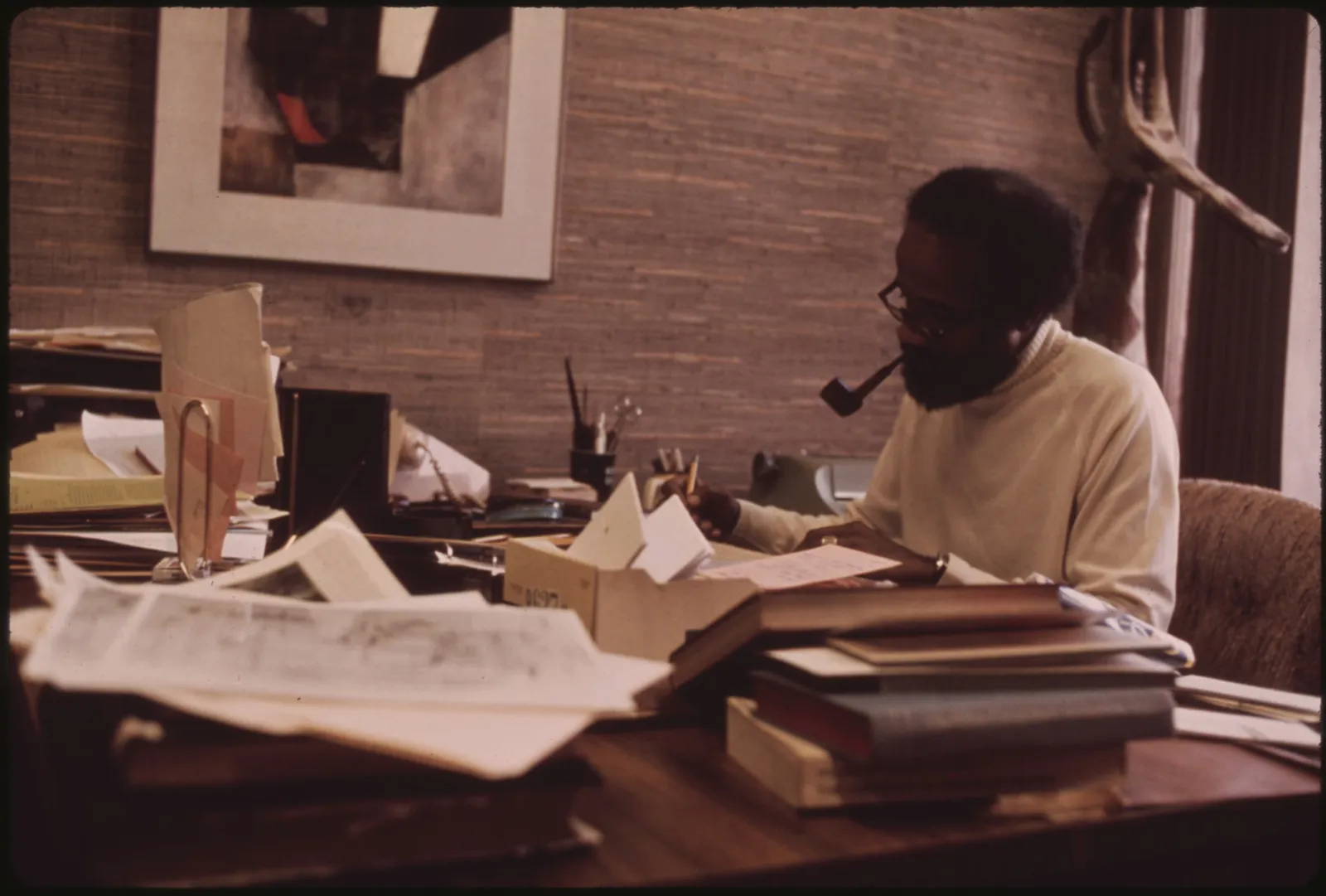 A black-and-white archival photograph of Lerone Bennett Jr., Ebony magazine's senior editor, seated at a desk working in his office inside the Johnson Publishing Company headquarters.