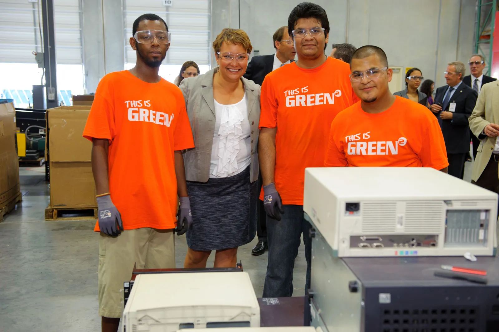 Lisa P. Jackson smiles alongside workers wearing safety glasses and 'This Is Green' T-shirts at the Round2 electronics recycling facility in July 2011.