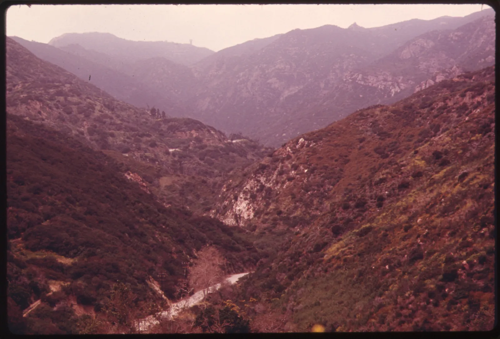 A wide view of the Malibu Canyon area of the Santa Monica Mountains near Malibu, California — dry, chaparral-covered hillsides under an open sky.