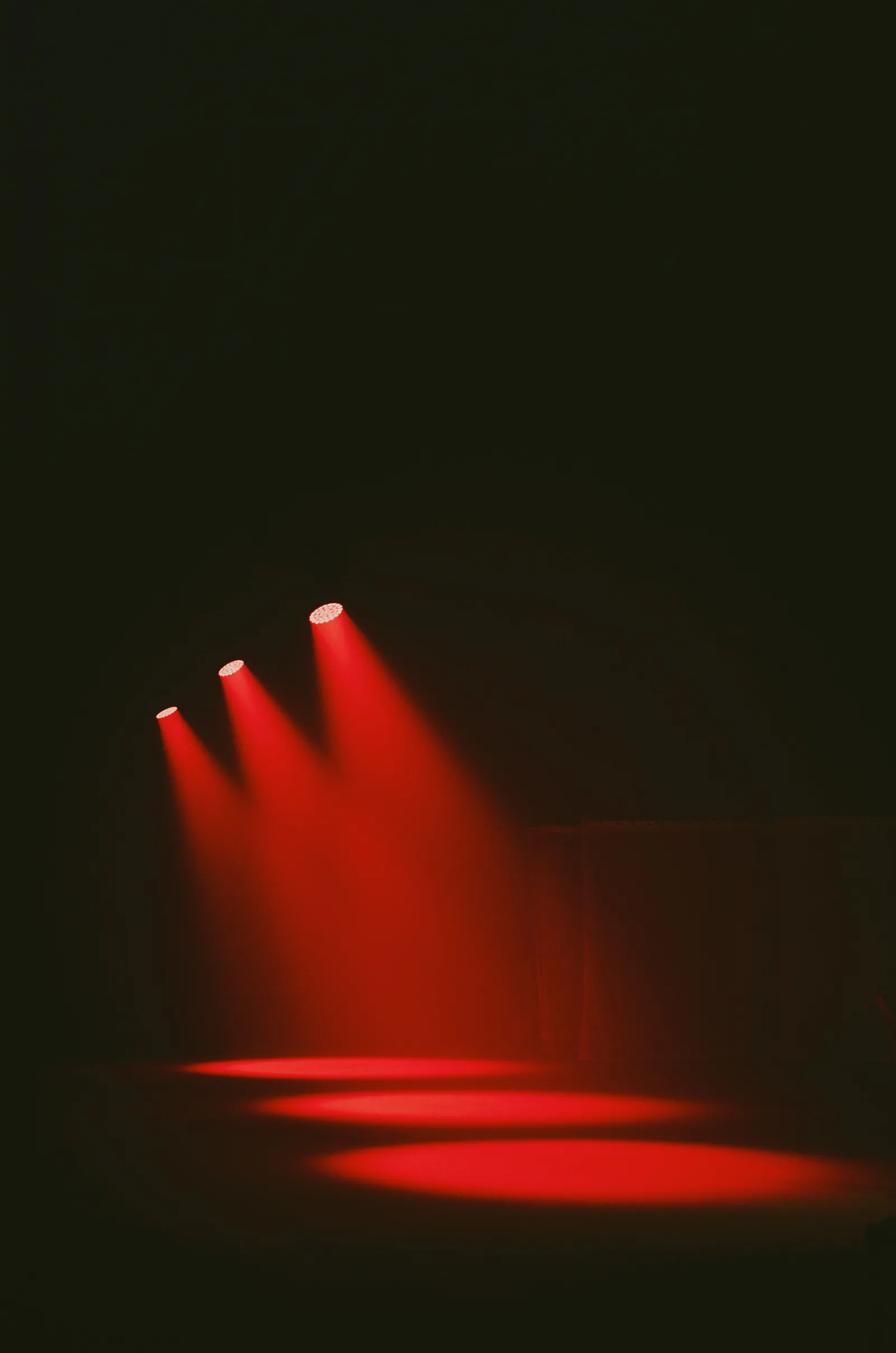 A dark, empty stage lit by three red spotlights, no performer or audience visible.