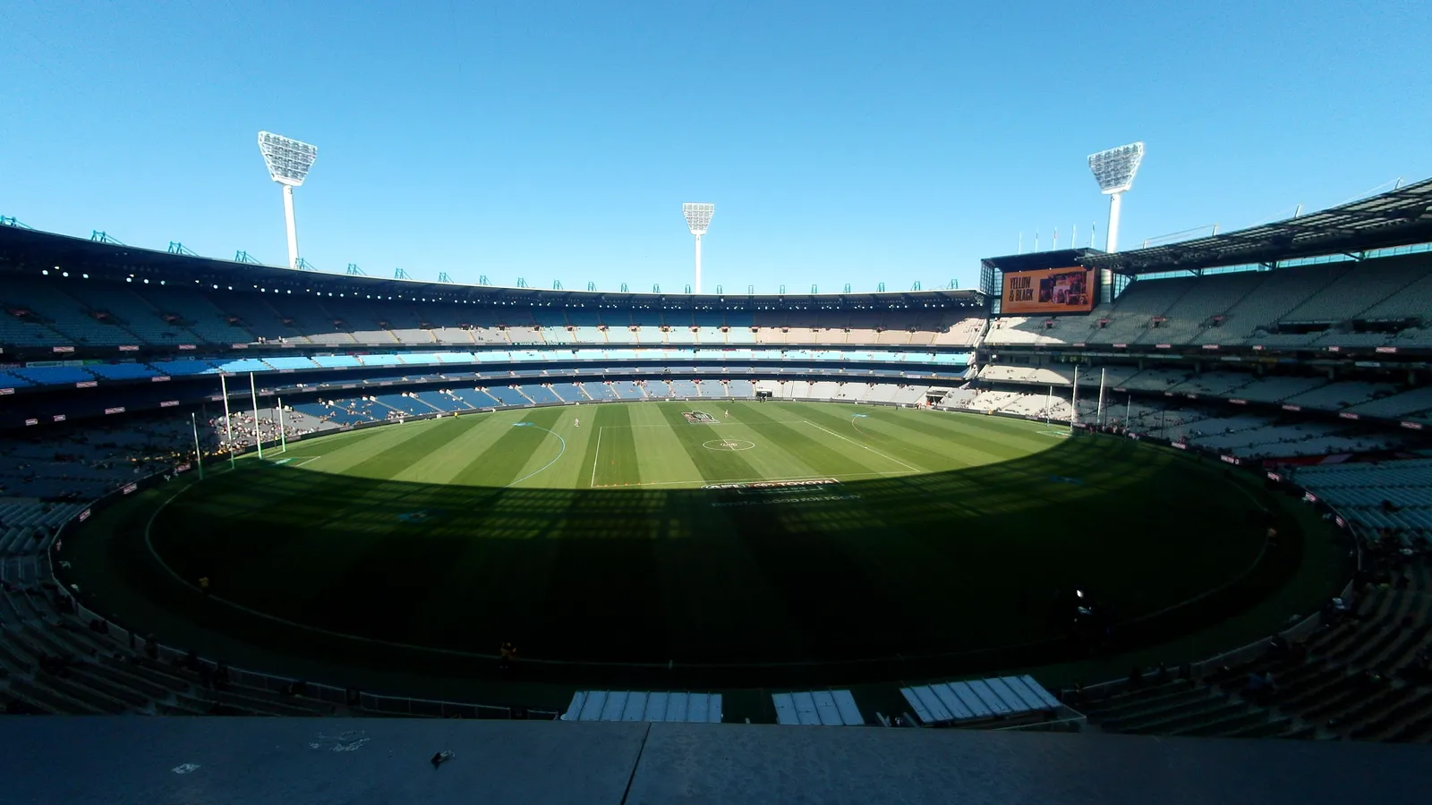 A panoramic view of the Melbourne Cricket Ground's empty grandstand bowl and light towers, seen from the upper deck, with the field marked out below ahead of a match.