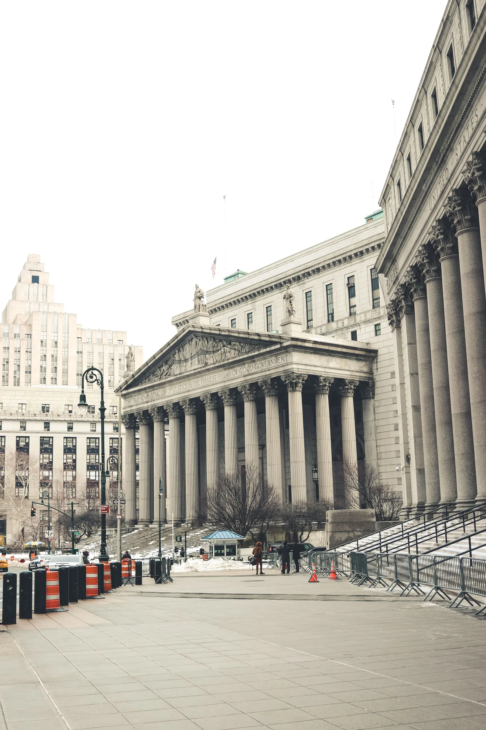 The New York County Courthouse in Manhattan, a neoclassical building fronted by a broad columned portico above a flight of steps, photographed from street level under a white, overcast sky.
