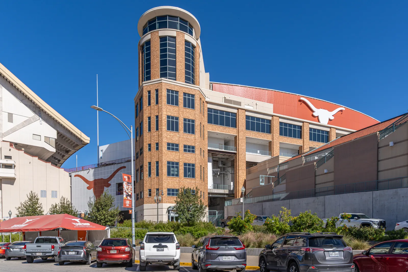 Ground-level exterior view of Darrell K Royal-Texas Memorial Stadium in Austin, home of the Texas Longhorns and tonight's Ohio State-Texas game — the stadium's brick entry tower and Longhorn logo seen from the parking lot on a clear day.