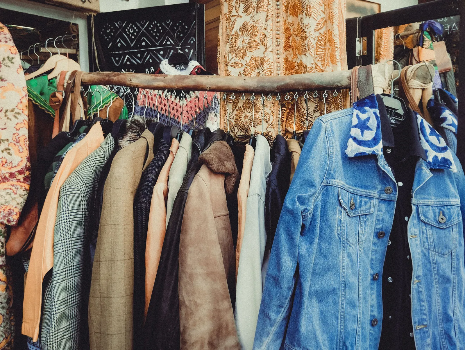 A row of vintage jackets in varied colors hanging on a wooden clothing rack inside a boutique. No people are visible in the frame.