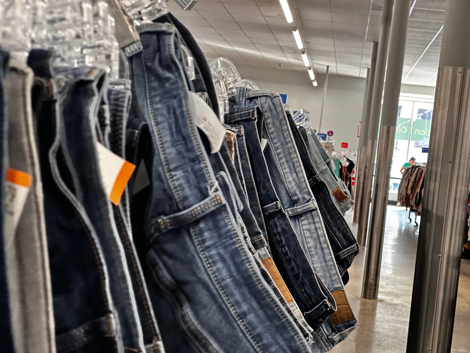 A rack of secondhand denim jeans on hangers inside a thrift store. No people are visible in the frame.