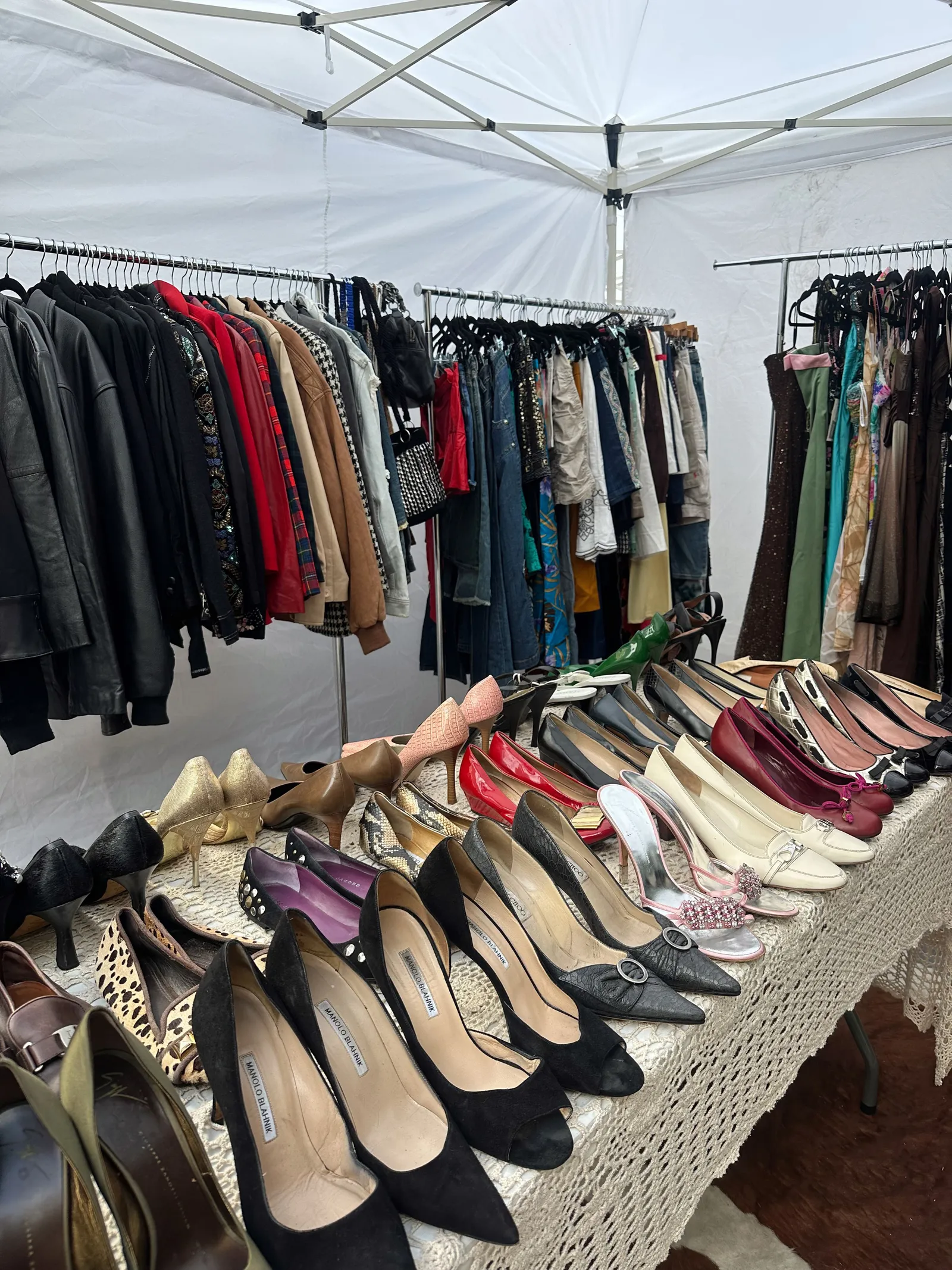 Colorful vintage clothes and shoes displayed on a table and rack at an outdoor market stall. No people are visible in the frame.
