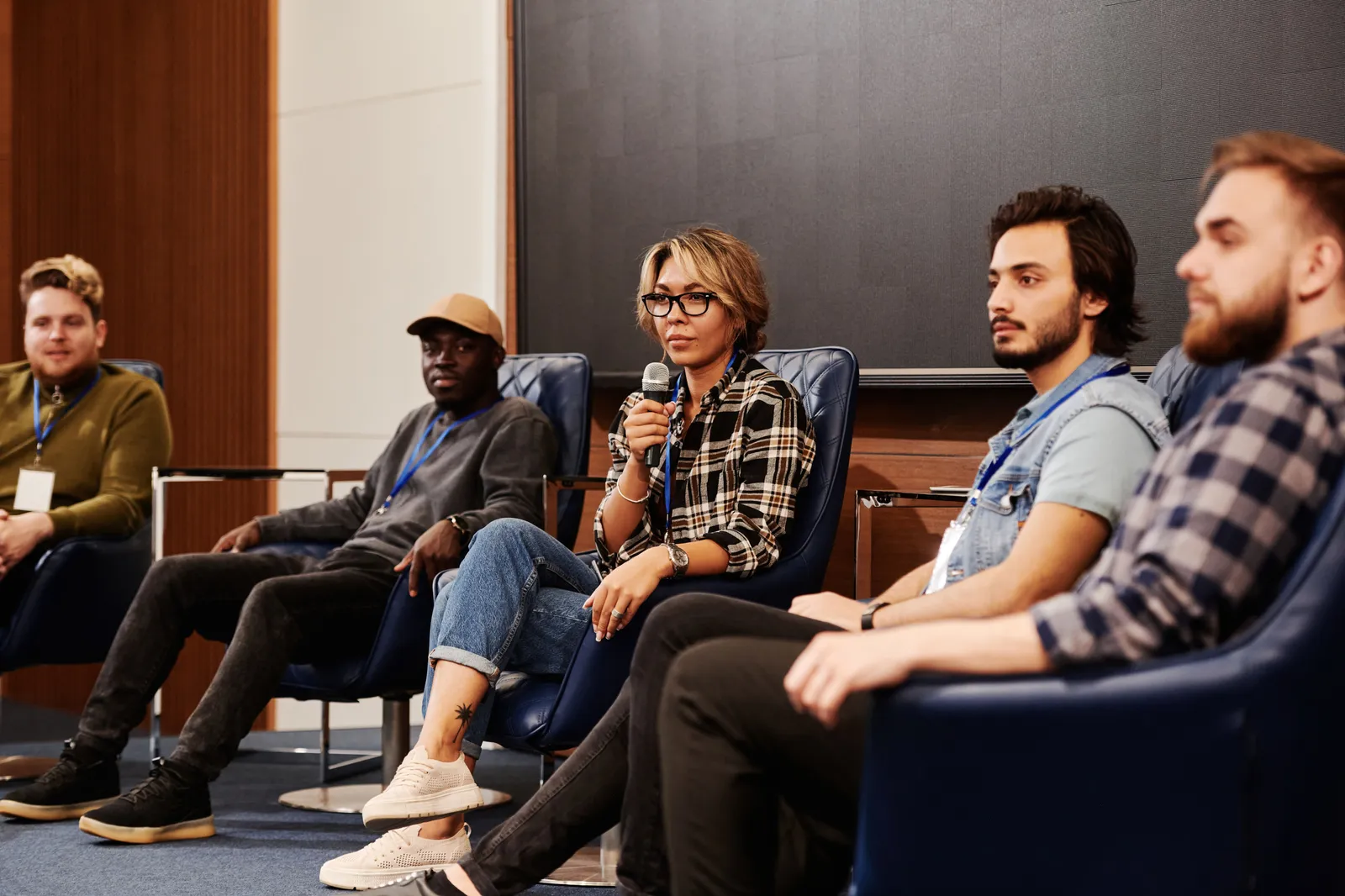 A diverse group of people seated on a panel at an indoor conference session, engaged in discussion.