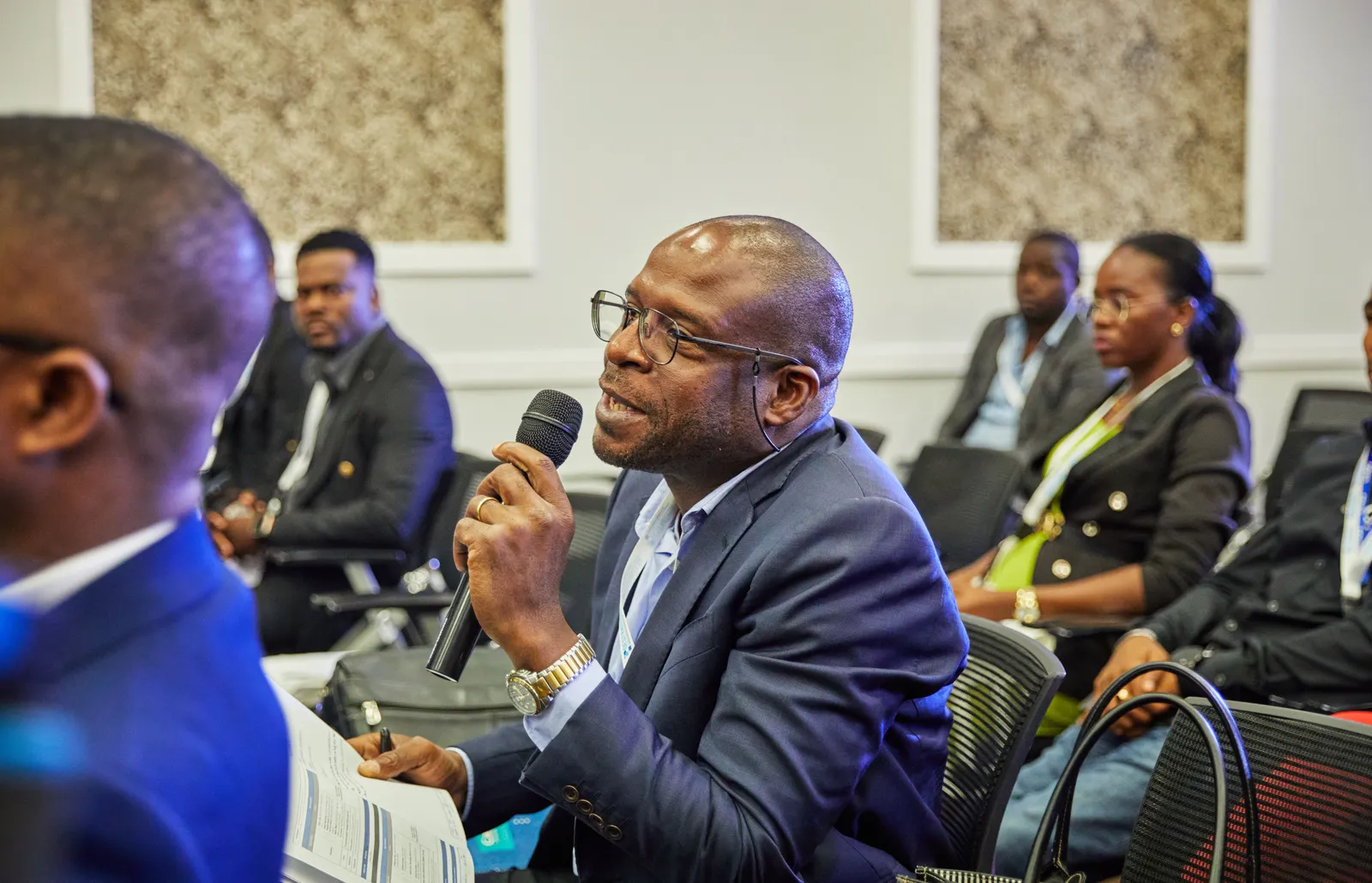 A conference attendee in a suit holding a microphone and asking a question from the audience.