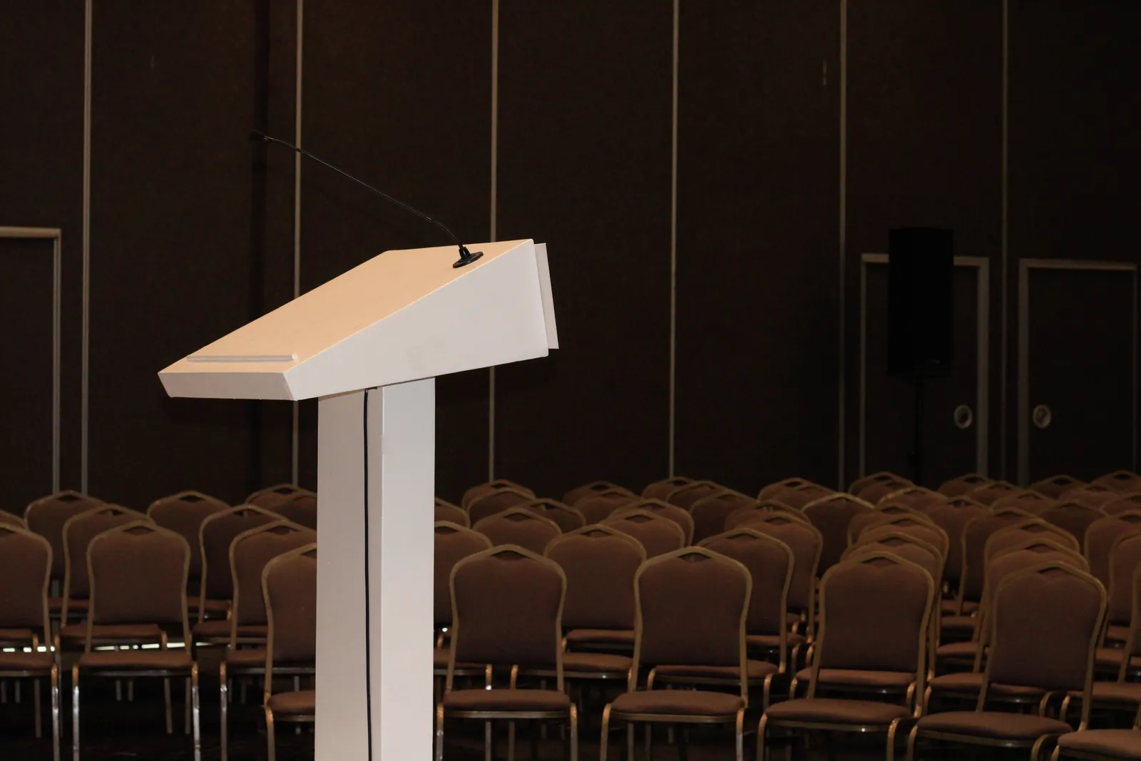 An empty conference ballroom with a lone podium and microphone facing rows of empty chairs, set up before or after a session.