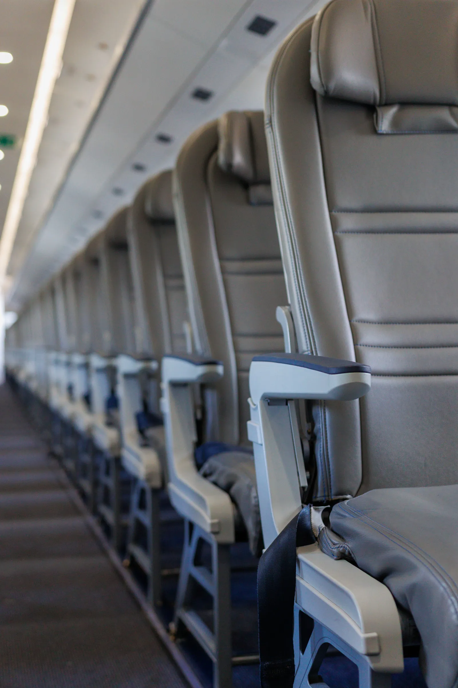 A view down the aisle of an empty economy cabin, identical grey seats receding toward the front of the aircraft with overhead bins closed above them.