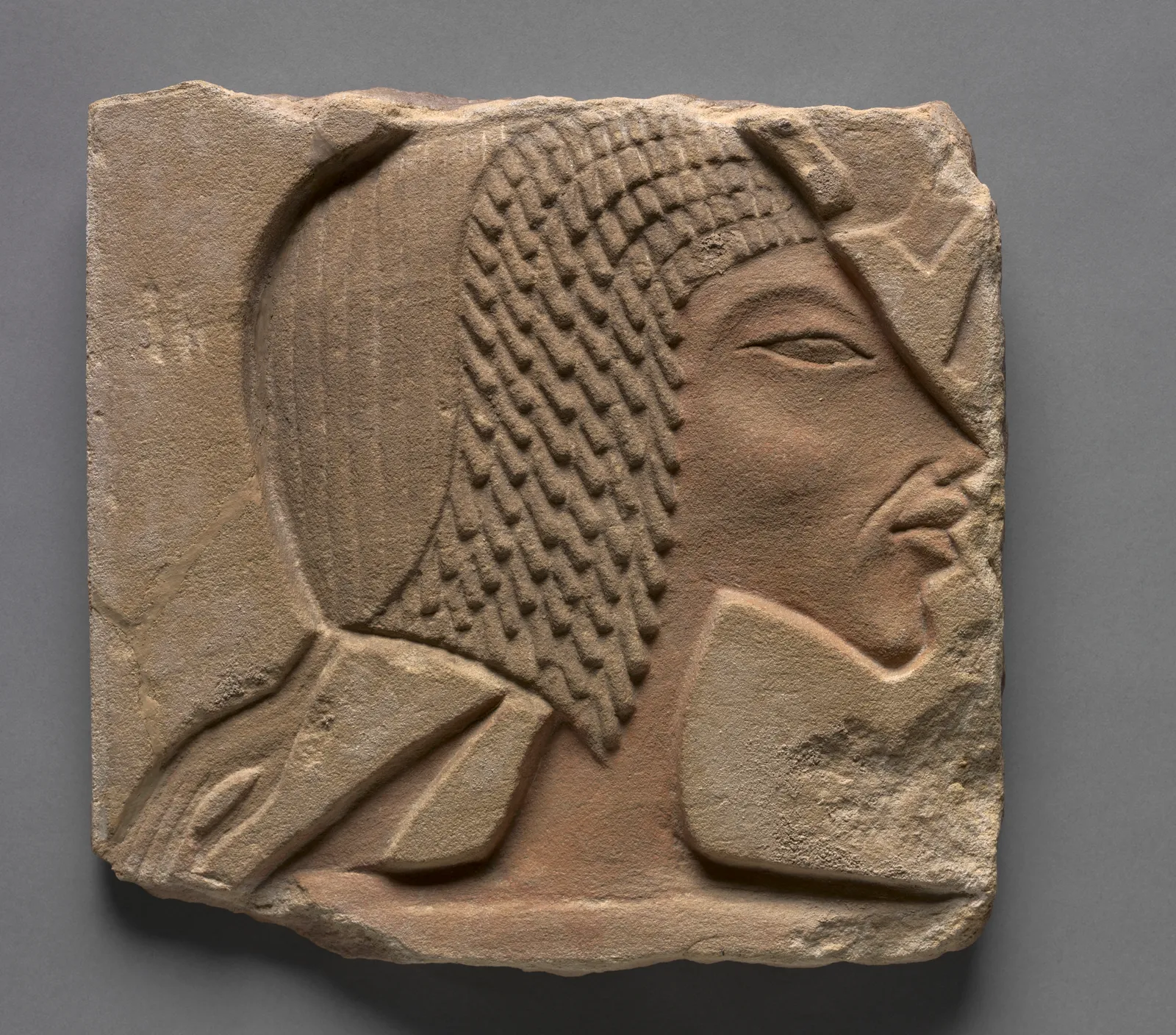 An Amarna-period sandstone talatat block carved in sunk relief with Nefertiti's profile, facing right, wearing a close-fitting cap-crown over a finely striated wig, the stone weathered to a warm pink-brown.