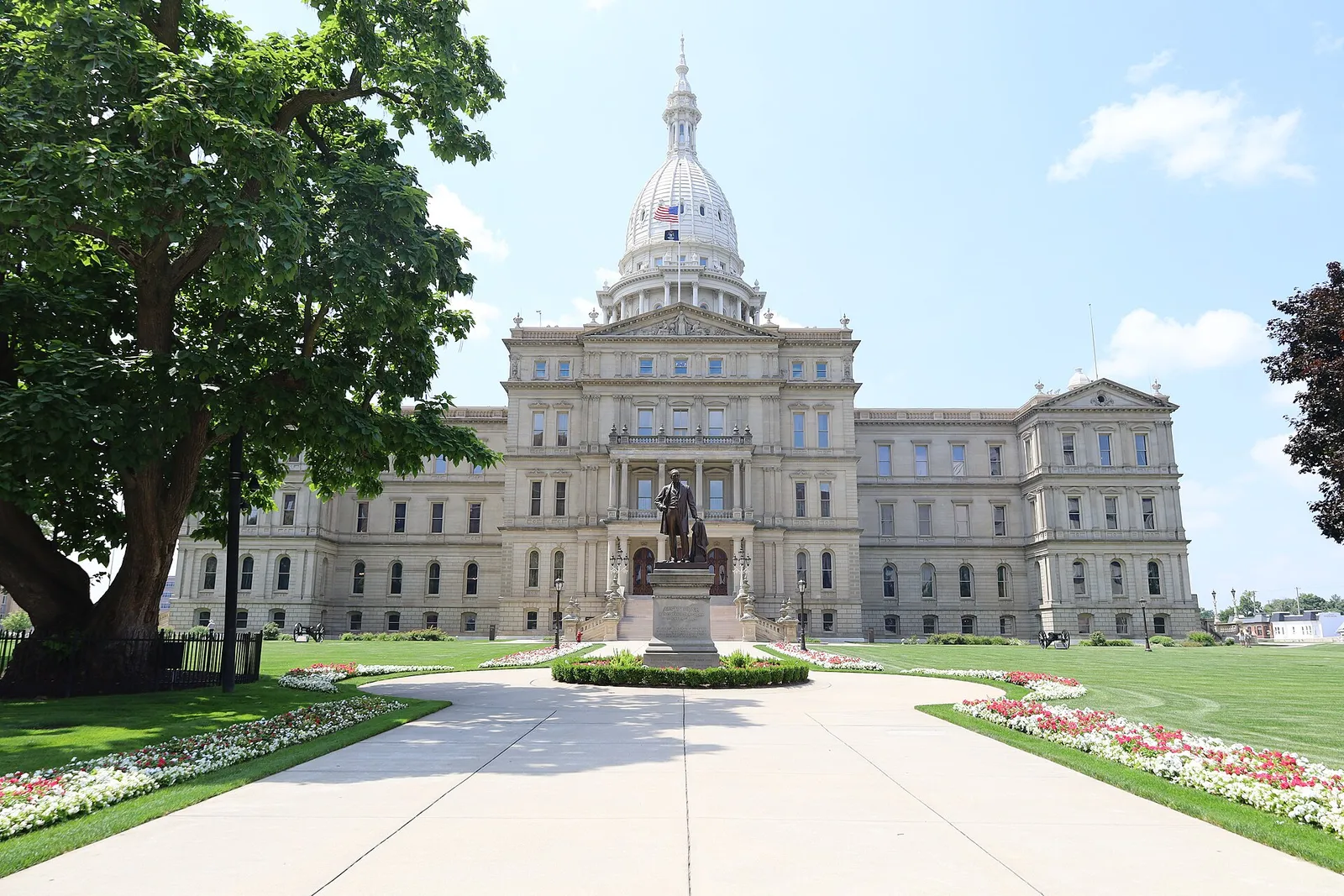 The Michigan State Capitol in Lansing on a clear summer day, its white cast-iron dome rising above the front lawn and flowerbeds — home of the only state ban.