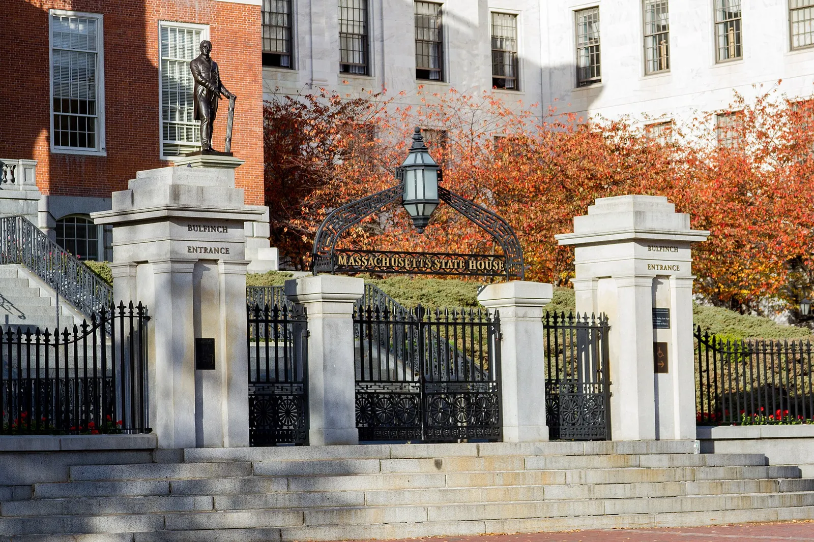 The wrought-iron Bulfinch Entrance gate of the Massachusetts State House in Boston, framed by granite pillars and autumn foliage.
