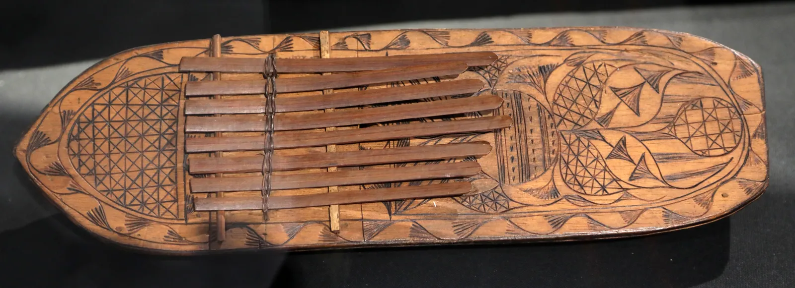A nineteenth-century Efik sanza, or agidigbo, from Old Calabar: an oval wooden soundboard covered in pokerwork geometric patterning, with a row of tuned metal tongues fixed across its centre.