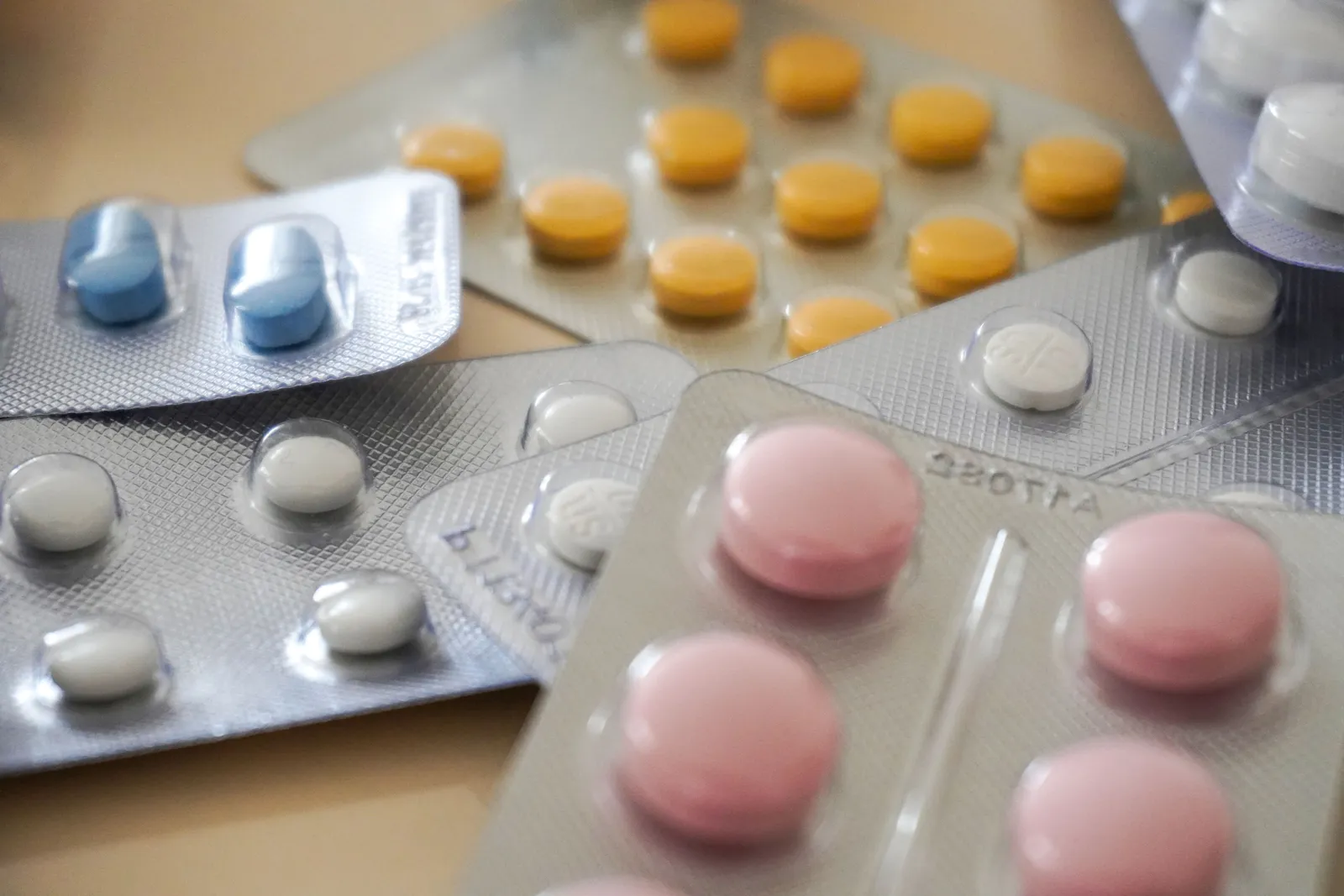 Close-up of several blister packs of assorted pills and tablets in different colors and shapes, spread on a table.